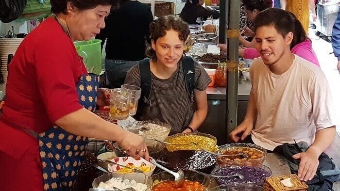 Two tourists are experiencing the dessert "che" at Dong Xuan Market in Hanoi